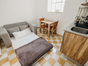 A compact room with a bed, a sofa, a small dining table with chairs, a kitchen area with a sink, and a window. - Bonito Mini loft Zona Centro SF (Guadalajara)