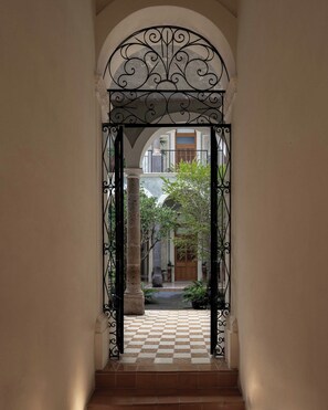 An arched doorway with a checkered floor leading to a courtyard with a wooden door and columns. - Bonito Mini loft Zona Centro SF (Guadalajara)