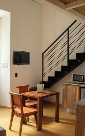 A dining area with a wooden table and chairs, a black staircase, and a microwave on a countertop. - Loft en el centro de Guadalajara LC (Guadalajara)