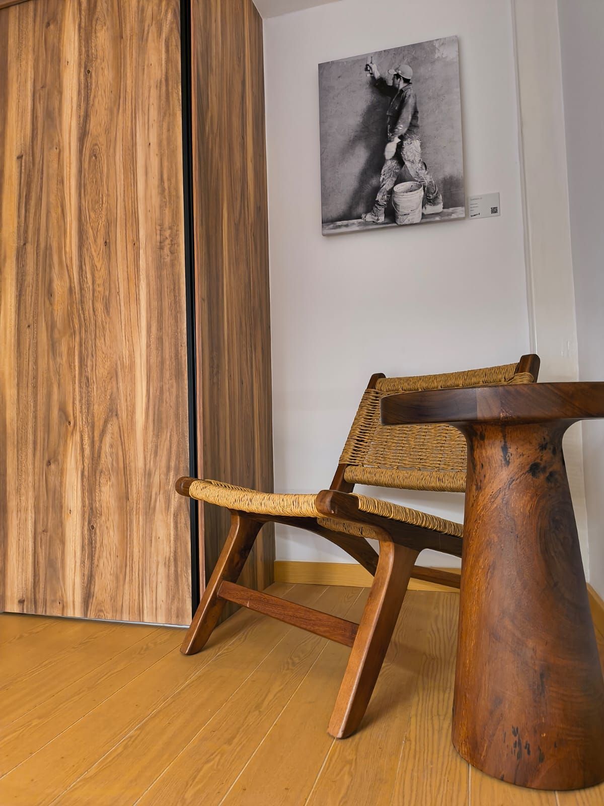 Un plancher en bois, une chaise en osier, une table en bois et un tableau en noir et blanc accroché au mur.