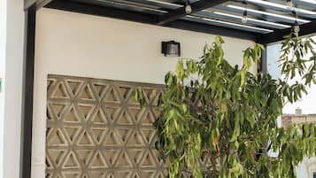 Een overdekt buitengebied met een wand met een geometrisch patroon, potplanten en een metalen dakconstructie.