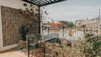 Een terras met een pergola, twee stoelen, een tafel en een uitzicht op gebouwen op de achtergrond.