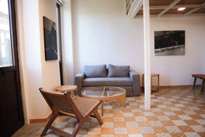 A room with a checkered floor, a grey sofa, a wicker chair, and a glass coffee table. - Suite Loft Guadalajara Centro SF (Guadalajara)
