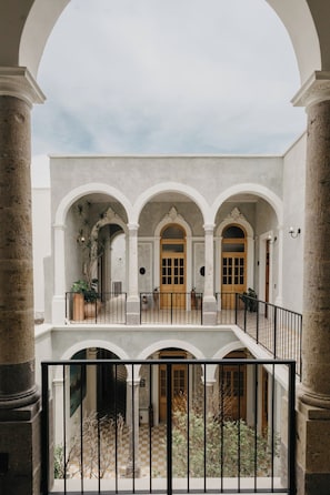 A courtyard with a central open area, surrounded by columns and arches, with a balcony overlooking the space. - Loft Estandar en Casona Restaurada GDL SF (Guadalajara)