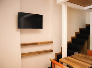 A modern interior with a flat-screen TV mounted on a wall, wooden shelves, a staircase, and a wooden table. - Loft Estandar en Casona Restaurada GDL SF (Guadalajara)