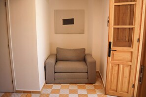 Quarto com sofá bege, porta de madeira e piso de azulejos.