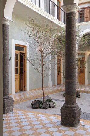 A courtyard with a tree, columns, and a checkered floor. - Loft Estandar en Casona Restaurada GDL SF (Guadalajara)