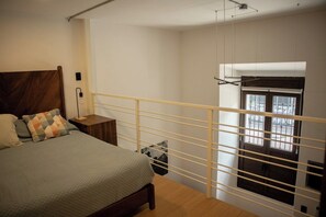A bedroom with a bed, nightstand, and a window with blinds. - Loft histórico en el corazón de GDL LC (Guadalajara)