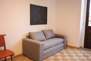 Ein Zimmer mit einem grauen Sofa, einem Holzstuhl und einem karierten Boden.