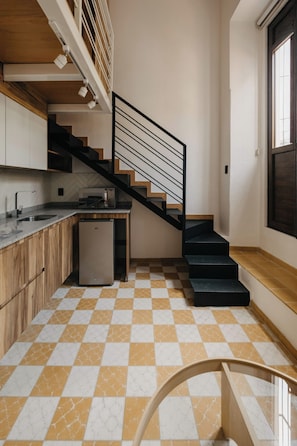 Eine Küche mit Schachbrettfußboden, einem Kühlschrank, einer Mikrowelle und einer Treppe mit schwarzer Geländer.
