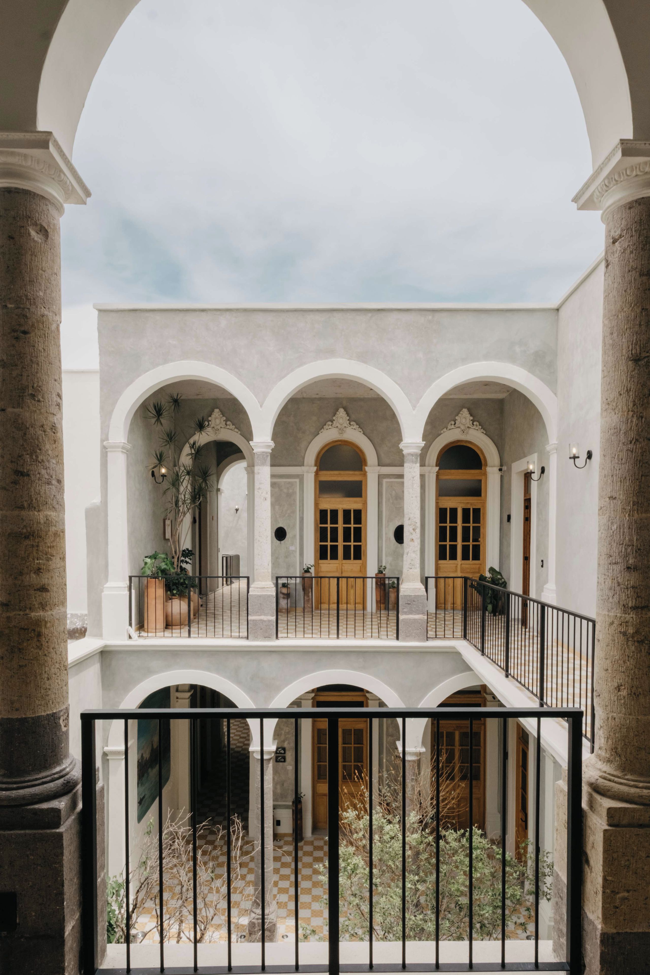 Une cour intérieure dotée d’un espace central ouvert, entourée de colonnes et d’arcades blanches, et agrémentée d’un balcon donnant sur cet espace.