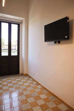 Ein Flur mit Fliesenboden, einer Tür und einem an der Wand befestigten Fernseher.