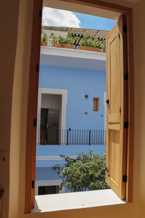 A view through an open wooden door into a building with a blue exterior, a balcony with plants, and a small window with a number. - Bonito mini loft en el corazón de Guadalajara LC (Guadalajara)