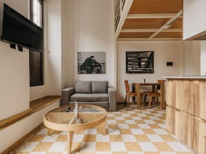 Een moderne leefruimte met een bank, een glazen salontafel, een eethoek met stoelen en een keukenblad.