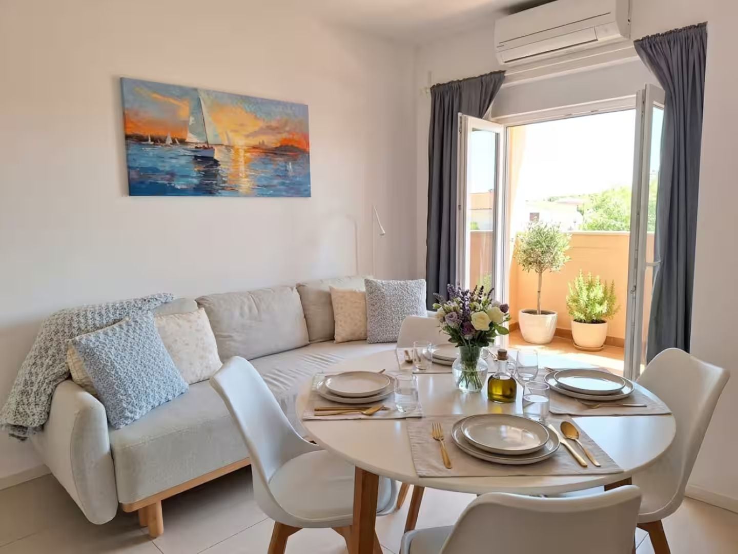 A dining area with a round table set for four, a sofa, and a painting above the table.