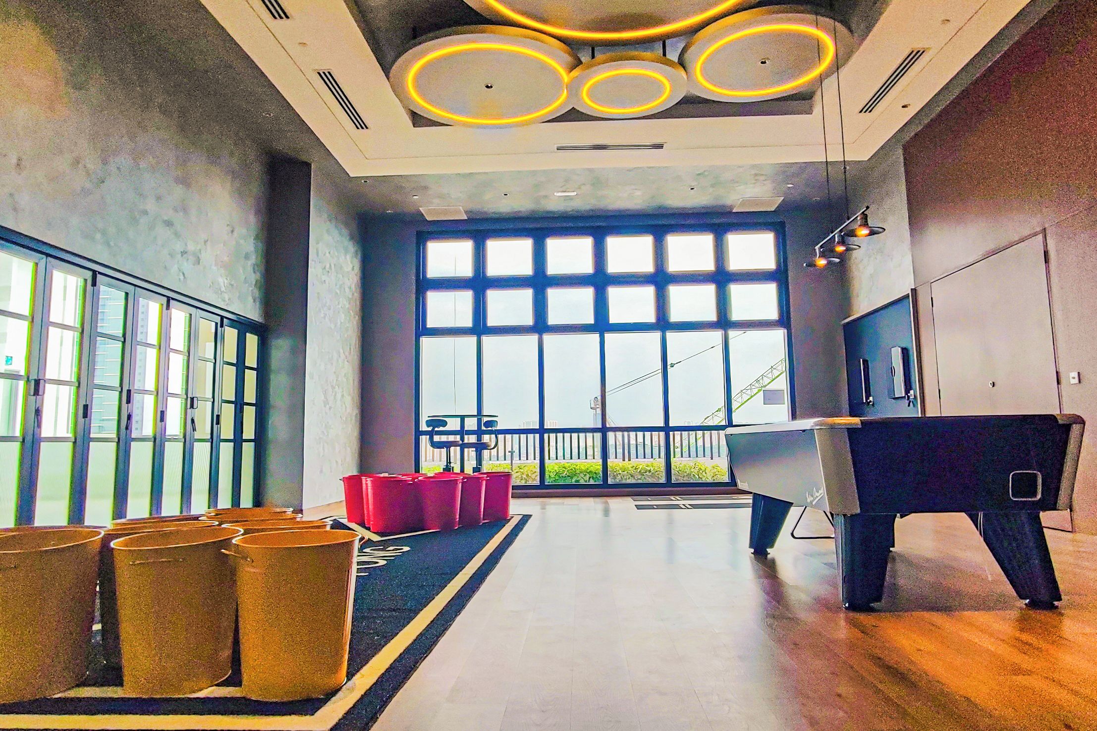Een ruime lobby met een groot raam, een pooltafel en diverse afvalbakken.