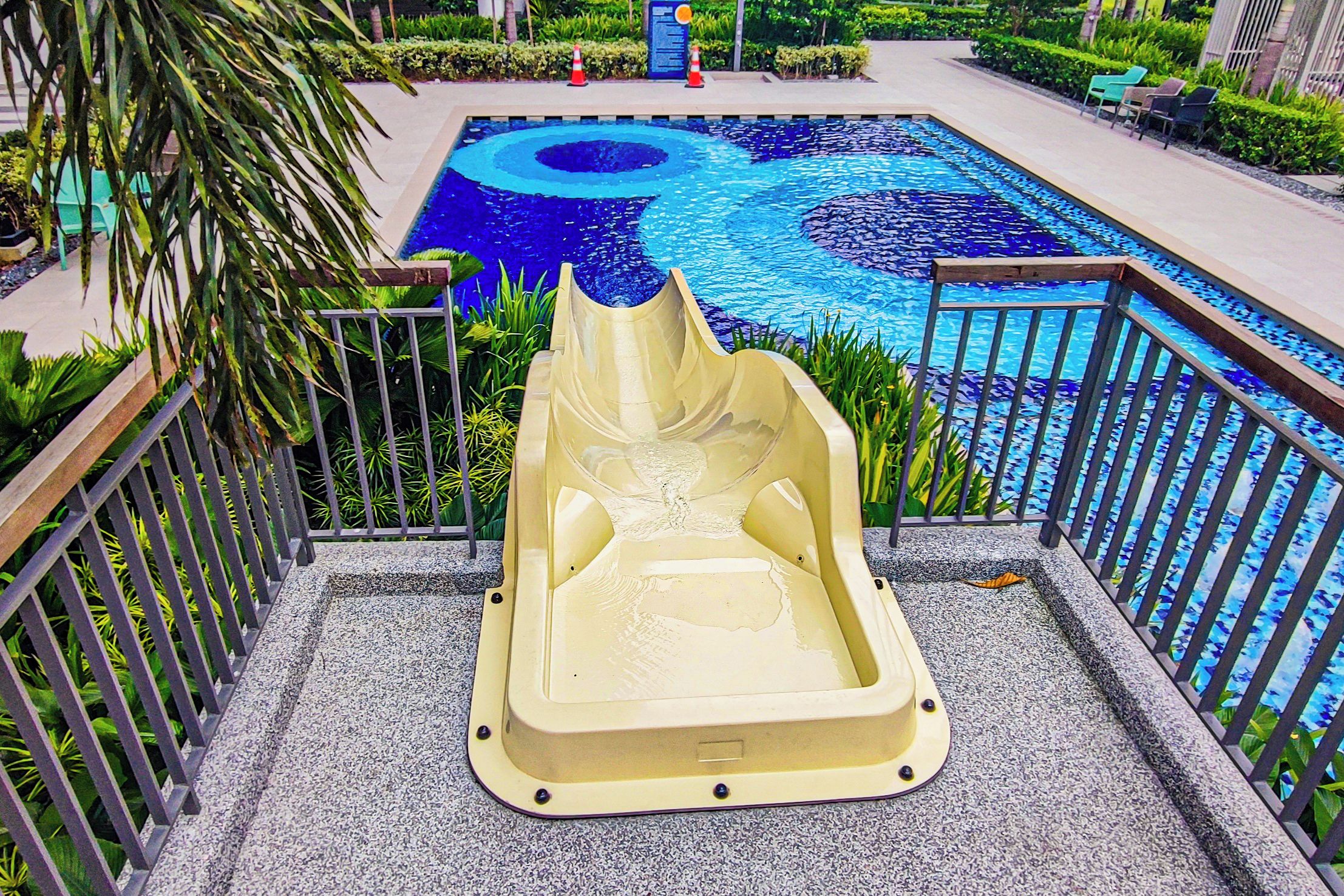 A pool with a unique design, surrounded by a metal railing and greenery.