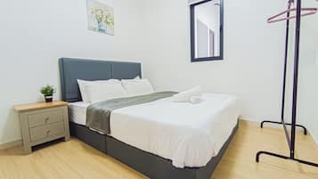 Een netjes opgemaakt bed met witte lakens en een grijs hoofdeinde, een nachtkastje met een plant, een klein schilderij aan de muur en een spiegel boven het bed.