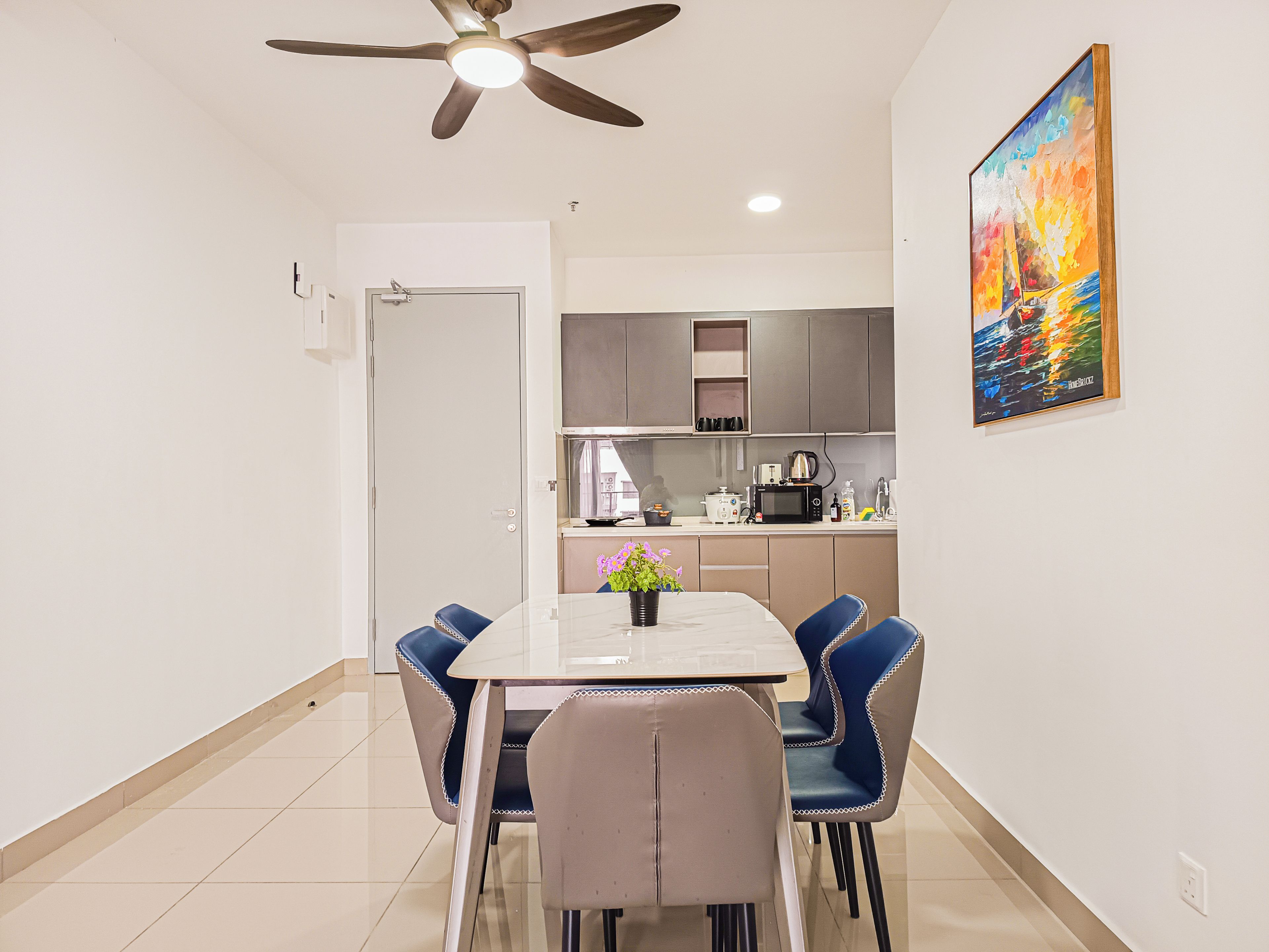 A modern kitchen with a dining area, a ceiling fan, and a painting on the wall.