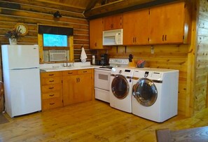 A compact kitchen with wooden cabinets, a refrigerator, a microwave, a stove, and a washing machine. - Cabin at Triangle Ranch near Badlands National Park. (Philip)