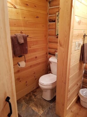 A wooden cabin bathroom with a toilet, a towel rack, and a roll of toilet paper. - Cabin at Triangle Ranch near Badlands National Park. (Philip)