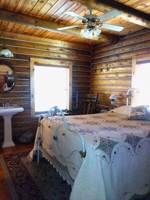 Una habitación tipo cabaña con una cama, un ventanal, un lavamanos y un ventilador de techo.