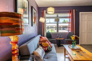 Ein Zimmer mit einer Couch, einem Tisch mit Blumen in einer Vase und einer Lampe.