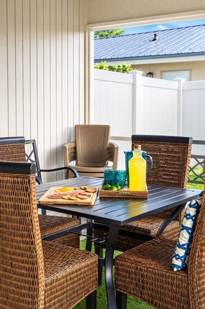 Eine Terrassengruppe im Freien mit Korbmöbeln, einem Tisch mit Speisen und Getränken und Blick auf ein Haus im Hintergrund.