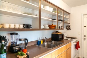 Eine Küche mit integriertem Mikrowellenherd, Toaster und Herd. Über der Arbeitsfläche befinden sich Regale mit Geschirr und Tassen.