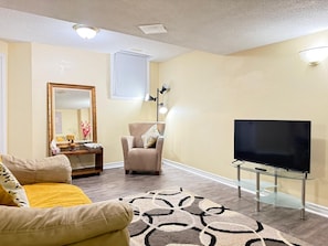 A living room with a sofa, armchair, TV, and a patterned rug. - Comfortable Basement Unit (Pickering)