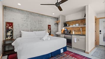 A hotel room with a bed, a ceiling fan, a small kitchenette, and a red patterned rug.