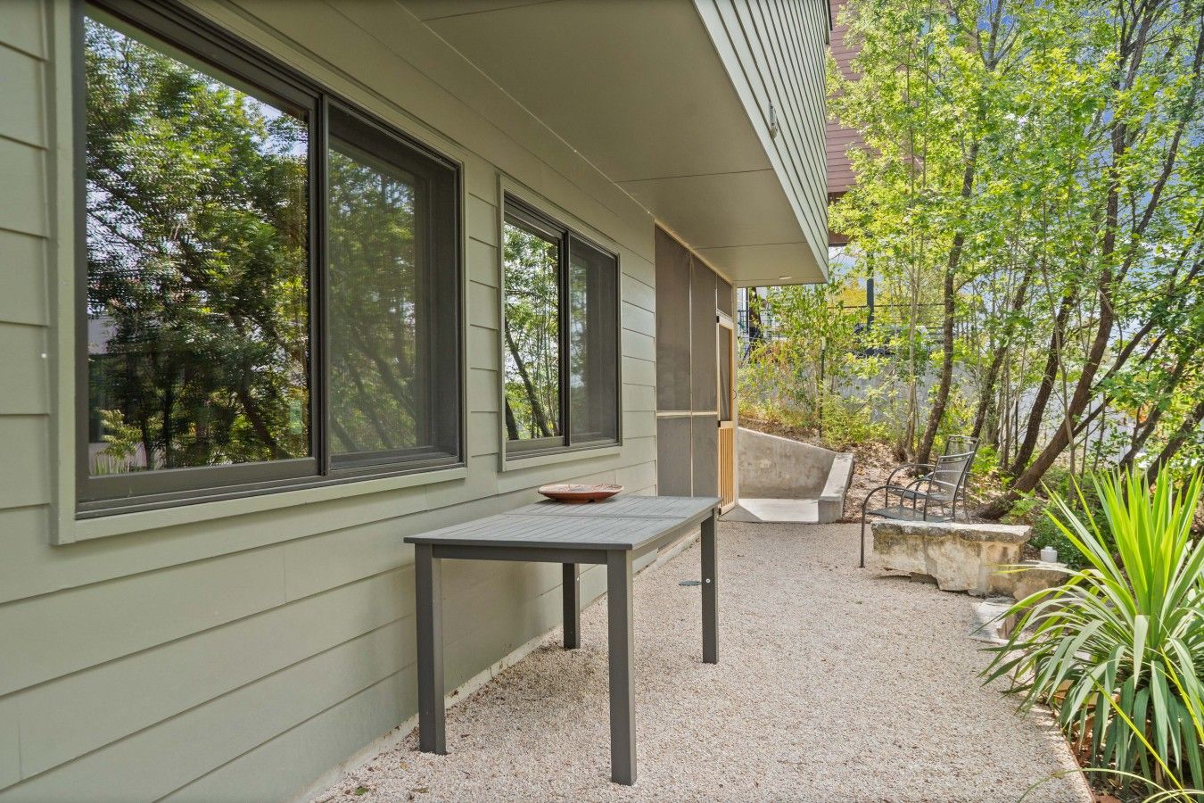 A patio with a table and chairs, a concrete planter, and a view of trees and a building.