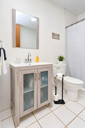 Ein Badezimmer mit Waschtisch aus Holz, einem Spiegel, einer Toilette und einer Duschvorhang.