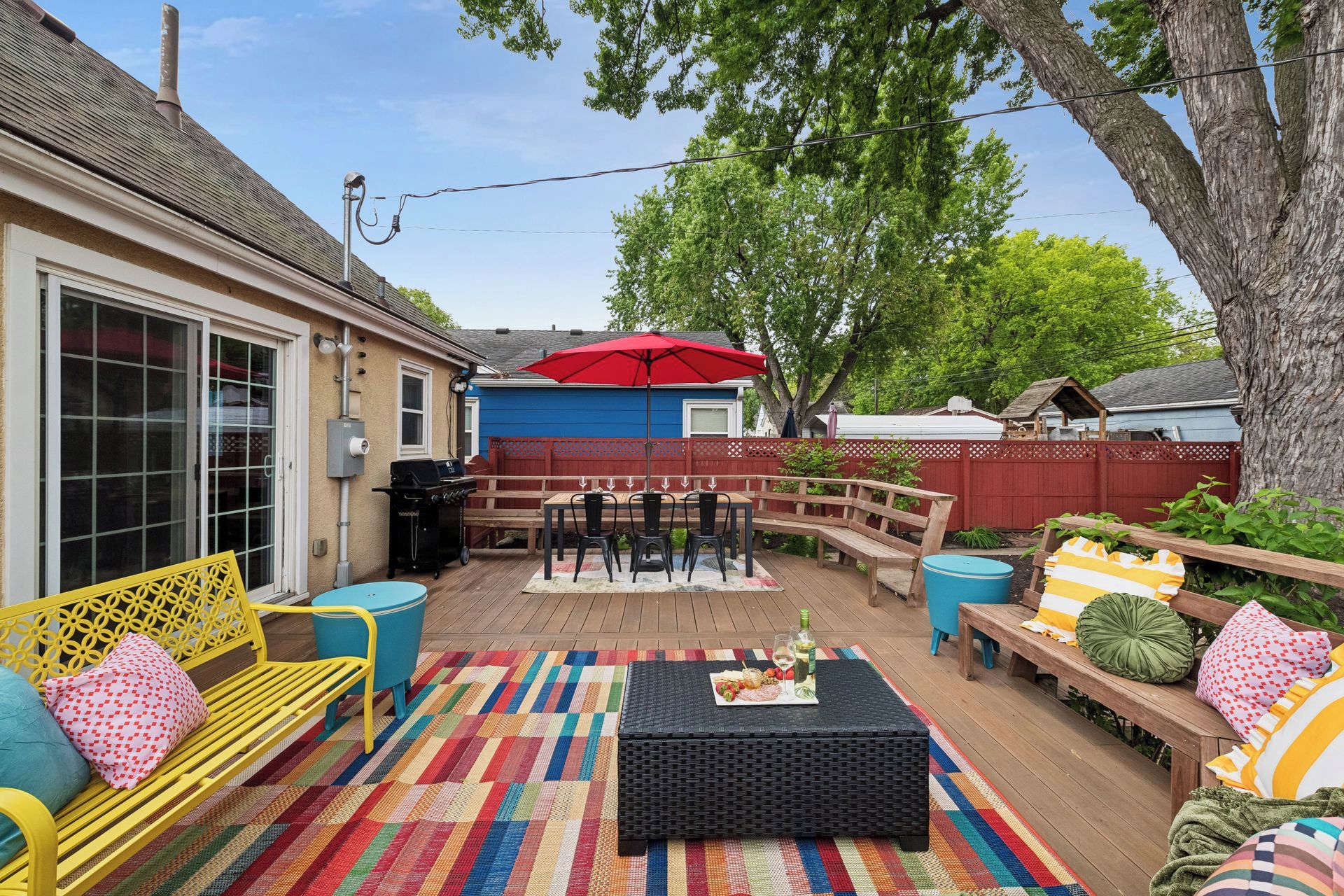 An outdoor patio with a dining table, chairs, a barbecue grill, and a red umbrella.