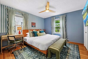 A bedroom with a bed, desk, chair, and a ceiling fan.
