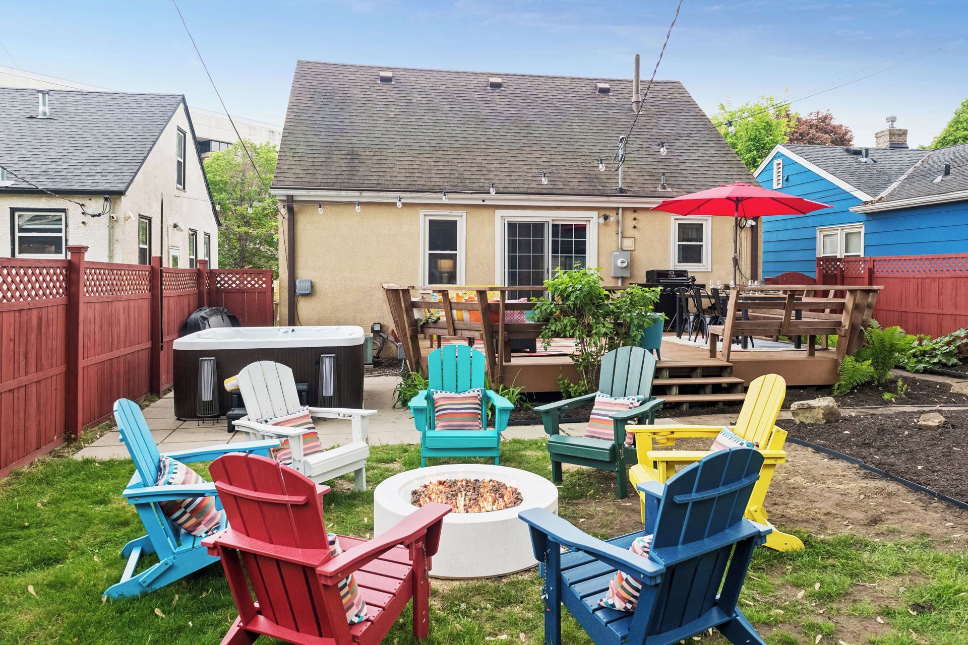 A backyard with a hot tub, fire pit, and outdoor seating area with Adirondack chairs.