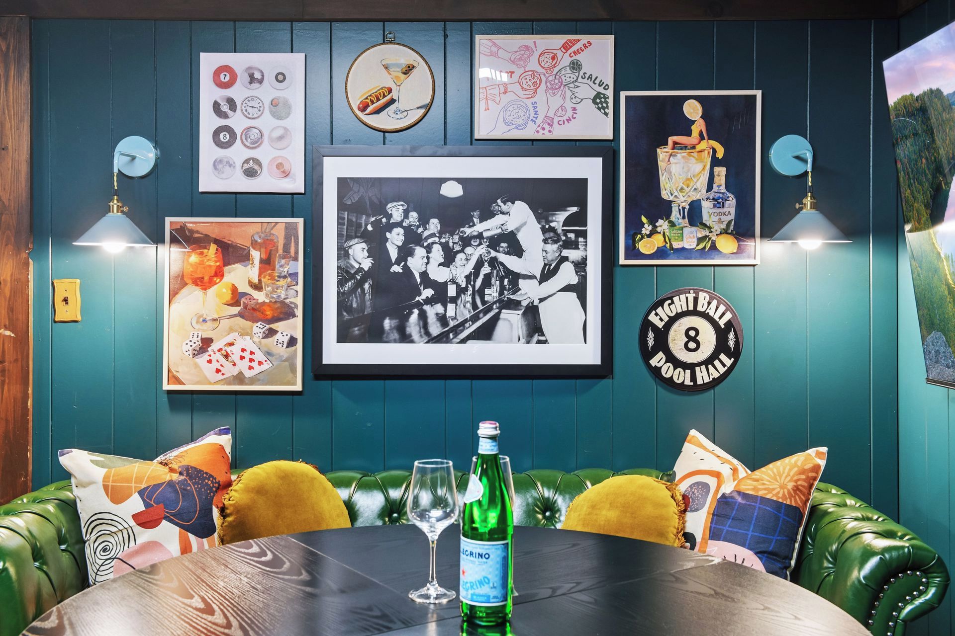 A room with a billiard table, green leather couch, and various framed pictures on the wall.