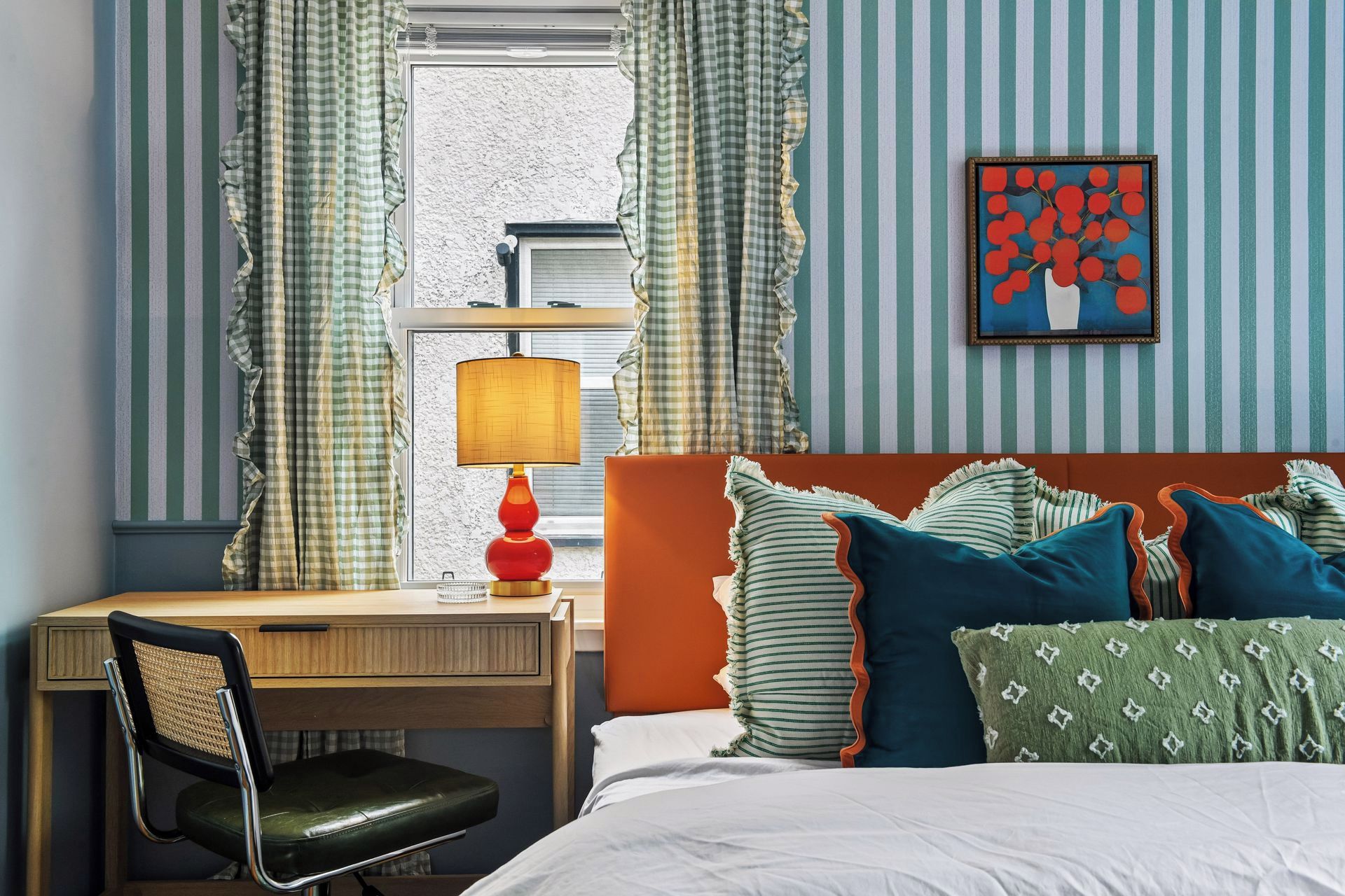 Quarto de hotel com cama, escrivaninha, cadeira, luminária e cortinas.