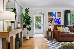 Un salon avec un plancher en bois, un canapé marron, une lampe, une plante en pot et une porte donnant sur l’extérieur.