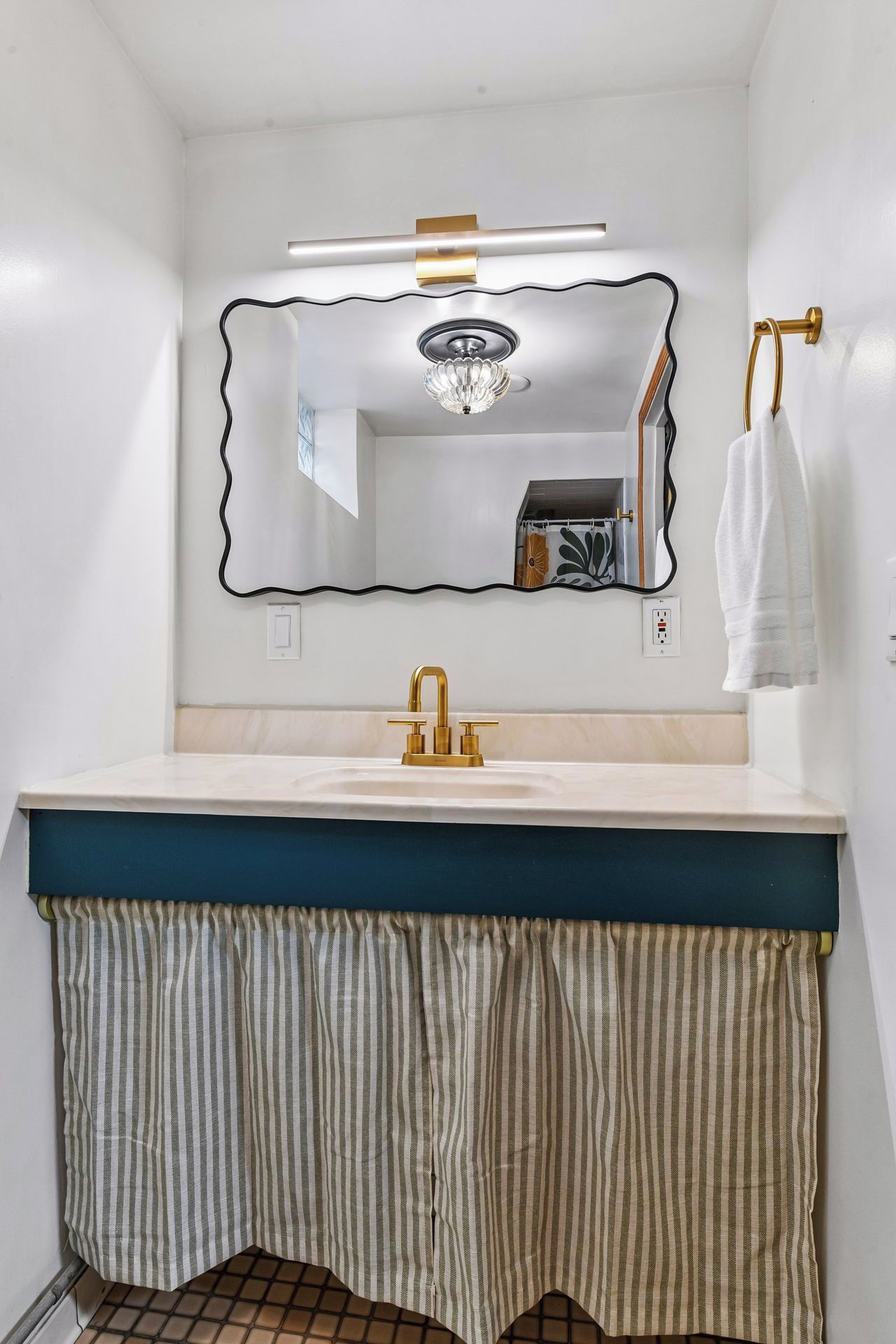 A bathroom with a white sink, gold faucet, and a mirror with a gold frame.