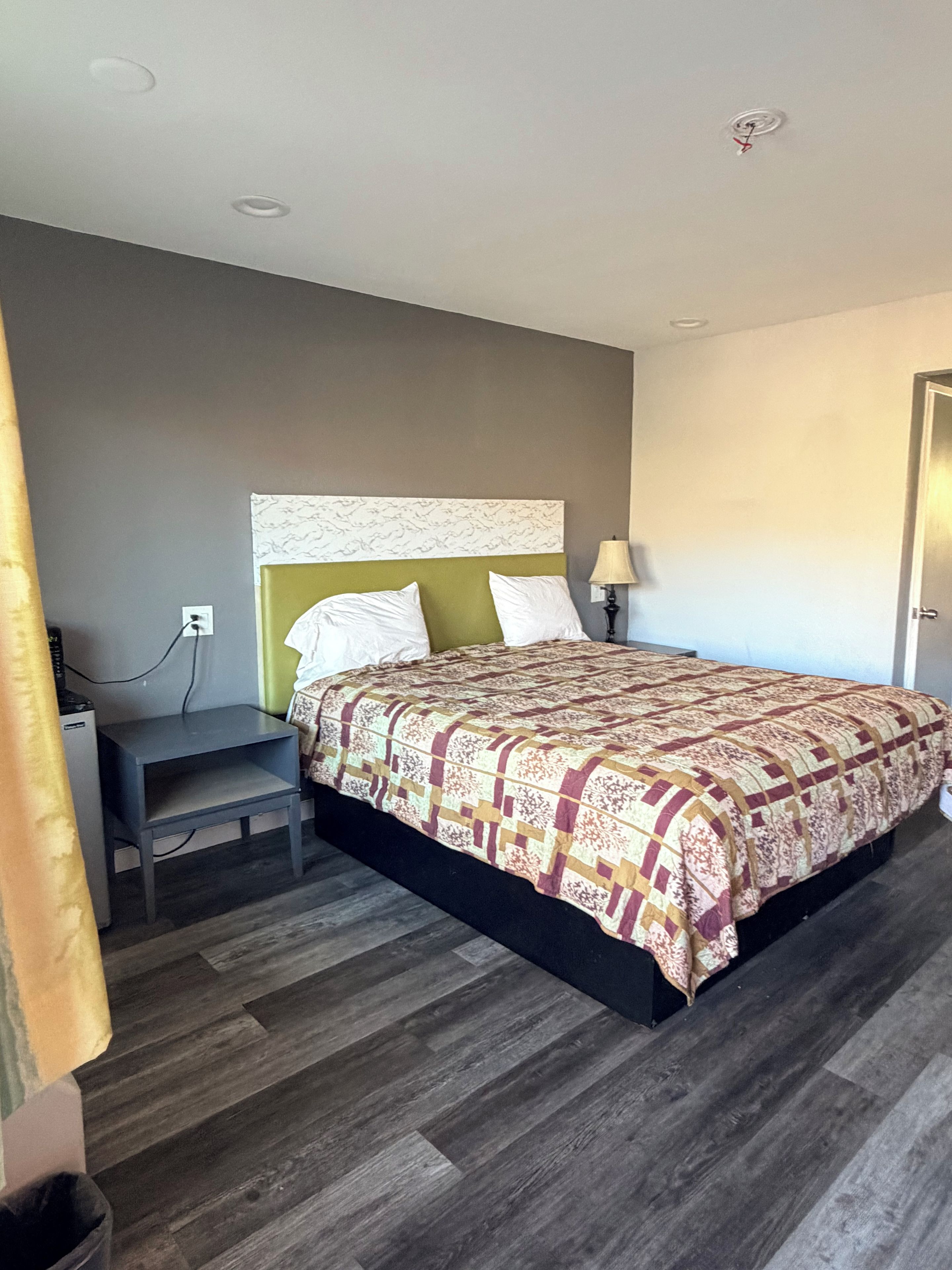 A hotel room with a bed, a bedside table, a lamp, and a power outlet.
