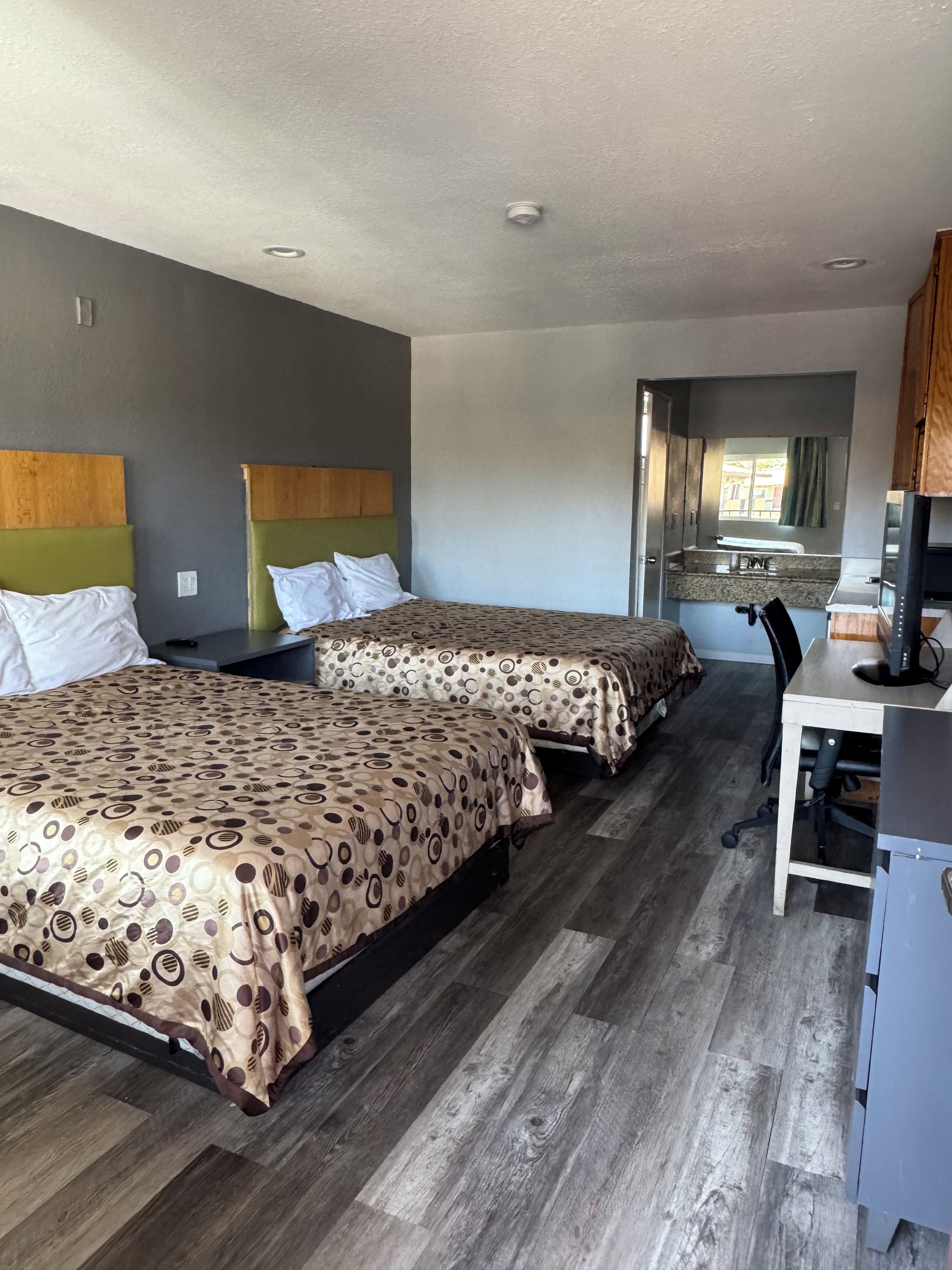 A hotel room with two beds, a desk, a computer, and a window.