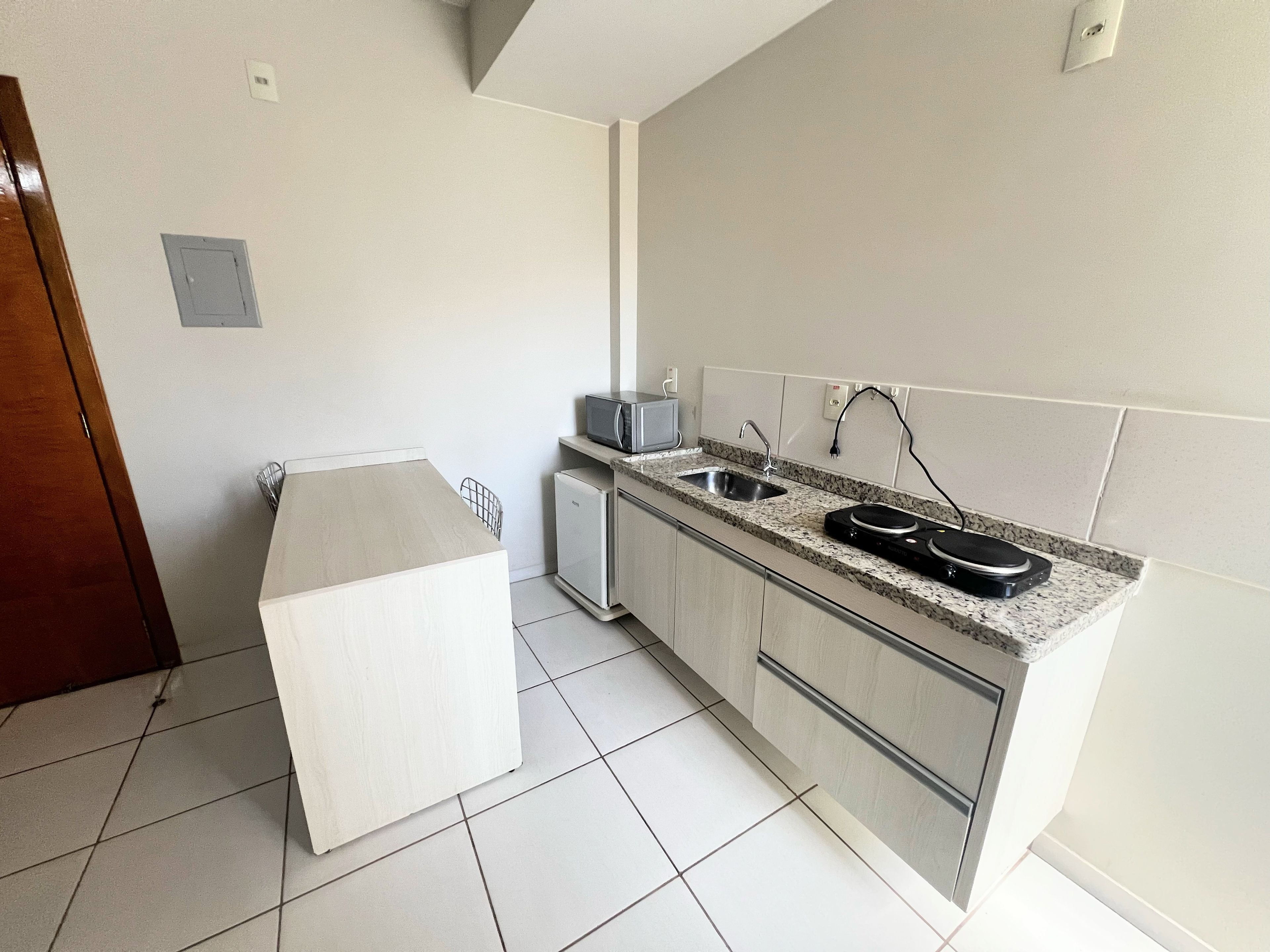 Una cocina moderna con microondas integrado, un lavamanos y un refrigerador compacto.