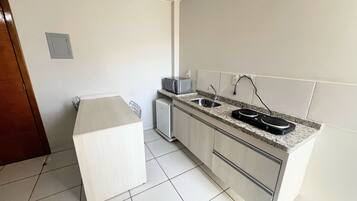 Una cocina moderna con microondas integrado, un lavamanos y un refrigerador compacto.