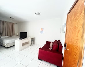 A hotel room with a bed, a TV on a white stand, a red sofa, and a wooden door. - CRCN - Golden Dolphin Supreme (Caldas Novas)