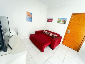 Una habitación con un sofá rojo, una puerta de madera y un escritorio blanco con una silla.