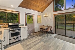 A modern kitchen with a large window, a dining area with a table and chairs, and a view of a forested area. - Cabin on Yakima River, Fish, Float, Golf, AC, BBQ (Cle Elum)