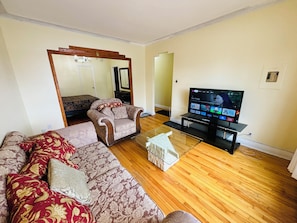 A living room with a sofa, armchair, TV, and a wooden floor.