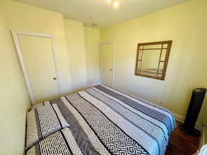 Ein Schlafzimmer mit einem Bett, einer Tür, einem Spiegel und einer Stehlampe.