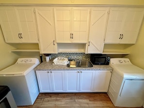 A compact kitchen with white cabinets, a granite countertop, a microwave, a sink, and a washing machine.